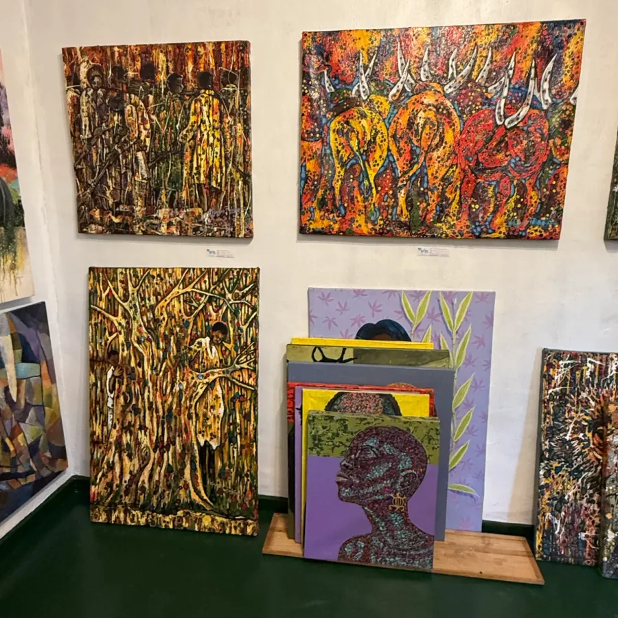 Gallery corner hung with colourful textured paintings of figures, long-horned cattle and trees, with more canvases stacked against the wall